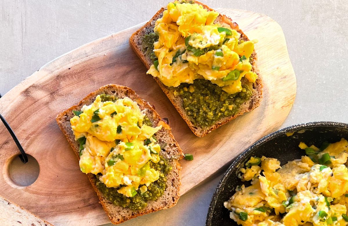 Rántotta kenyérszeleteken, Vilgain Vegán Pesto Genovese szósszal megkenve, fából készült deszkán tálalva, egy kis adag extra rántottával.